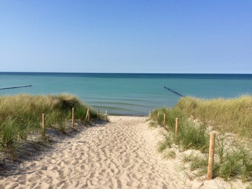 Sandweg zwischen Dünen zum ruhigen, blauen Wasser des Sees.