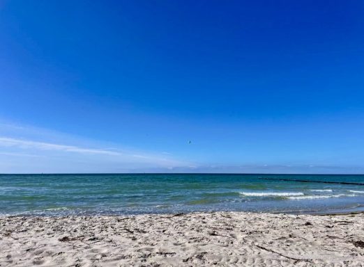 Strand mit feinem Sand und klarem Wasser unter einem strahlend blauen Himmel.
